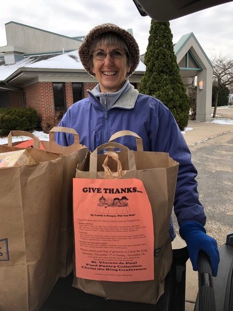 A volunteer standing in front of a table of brown grocery bags for a food drive.
