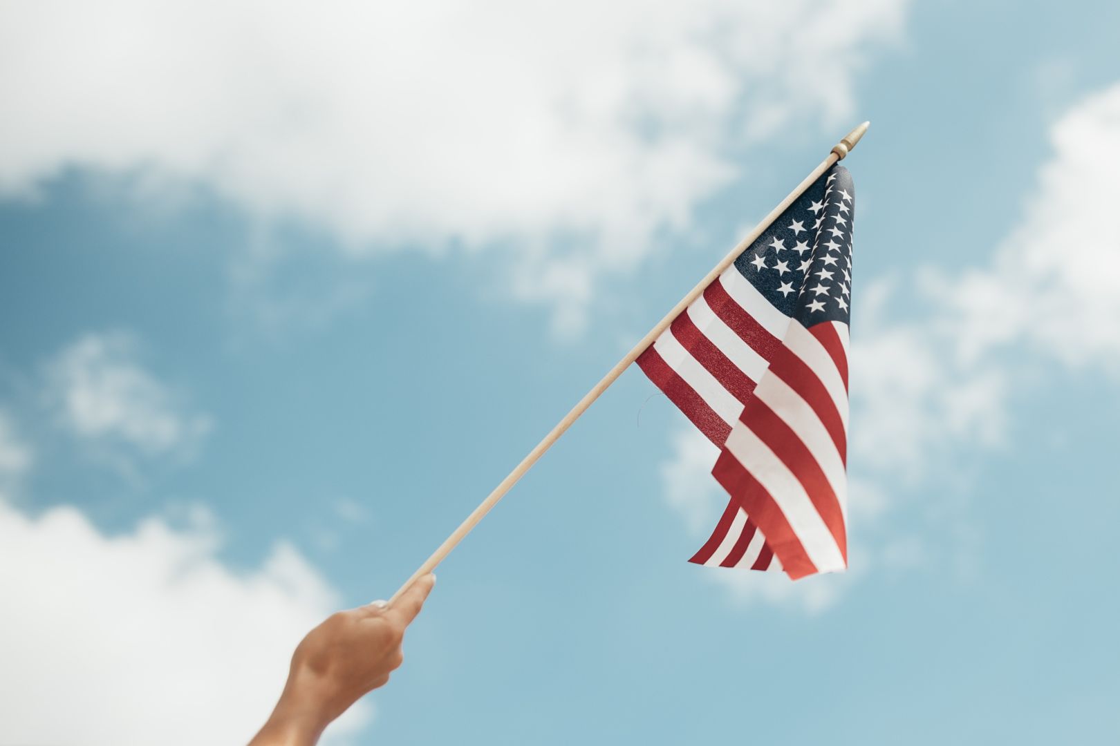 An American flag on a stick in front of a blue sky with clouds.